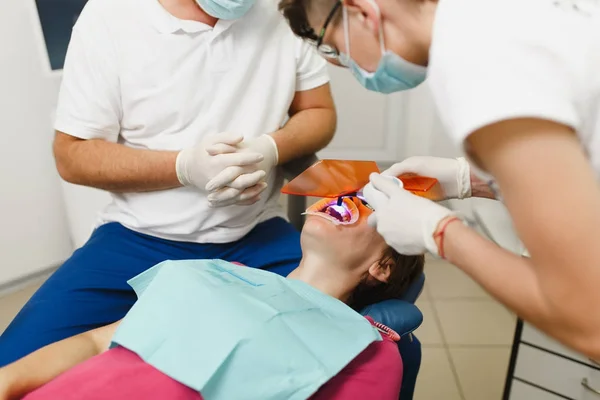 Processen för tandblekning UV-lampa med fotopolymer sammansättning. Professionell tandläkare och kvinnlig assistent hjälper behandla tänderna av kvinnlig patient på klinik ljus kontor med moderna verktyg utrustning. — Stockfoto