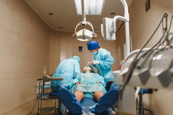 Manliga gamla professionell tandläkare kirurg i uniform och kvinnlig assistent hjälper till att utföra drift installera tandimplantat tänder av kvinnlig patient på klinik ljus kontor med moderna verktyg utrustning. — Stockfoto