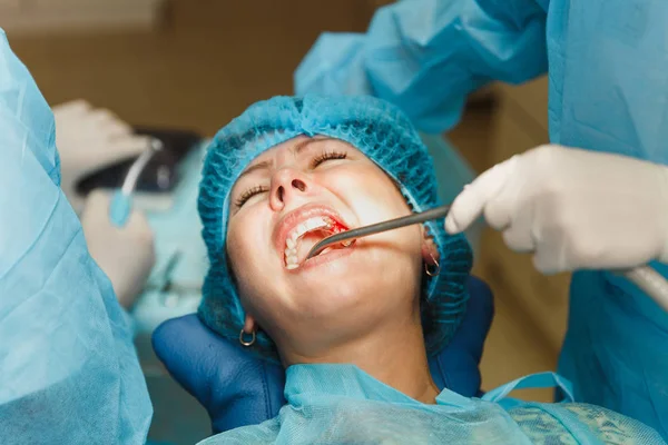Nära upp processen för manliga professionella tandläkare kirurgen utför åtgärden installera tandimplantat tänder av kvinnlig patient klinik ljus kontor med moderna verktyg utrustning. Blod och smärta i ansiktet. — Stockfoto