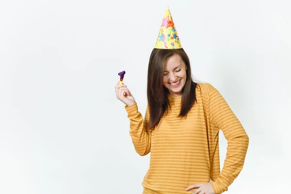 Mooie Kaukasische plezier gelukkig jongedame in gele kleding en verjaardag feest hoed met bruine lange haren, spelen pijp, vieren en te genieten van vakantie op witte achtergrond geïsoleerd voor advertentie. — Stockfoto