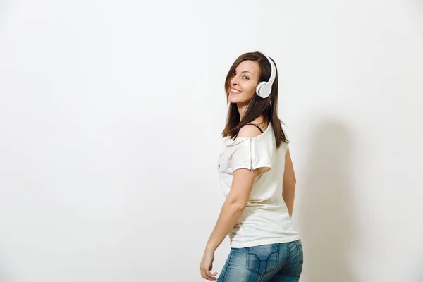 Hermosa joven europea emocional mujer morena feliz con una piel sana y limpia y una sonrisa encantadora, vestida con ropa ligera informal, escucha y disfruta de la música en los auriculares sobre un fondo blanco . —  Fotos de Stock