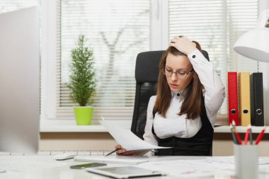 Takım elbise ve tablet ile masaya oturan gözlük güzel ciddi ve dalmış Kahverengi saç iş kadını ışık Office belgeleri ile modern monitör bilgisayarda çalışan bir kenara arıyorsunuz