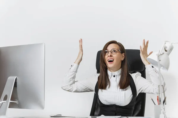 Frustrated angry business woman sitting at the desk, working at computer with documents in light office, swearing and screaming, holding hands up on white background, copy space for advertisement