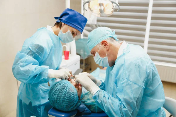 Üniforma ve kadın asistanı erkek eski profesyonel diş hekimi cerrahı Kliniği hafif ofis modern araçlar ekipman ile işlem yükleme diş implant diş kadın hastanın gerçekleştirmek için yardımcı olur.