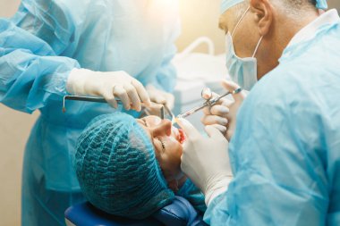 Üniforma ve kadın asistanı erkek eski profesyonel diş hekimi cerrahı Kliniği hafif ofis modern araçlar ekipman ile işlem yükleme diş implant diş kadın hastanın gerçekleştirmek için yardımcı olur.
