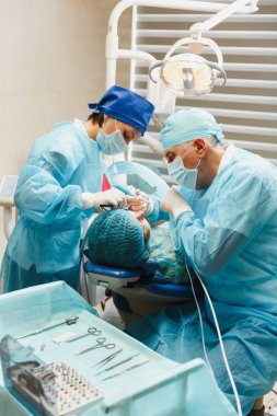 Üniforma ve kadın asistanı erkek eski profesyonel diş hekimi cerrahı Kliniği hafif ofis modern araçlar ekipman ile işlem yükleme diş implant diş kadın hastanın gerçekleştirmek için yardımcı olur.