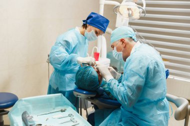 Üniforma ve kadın asistanı erkek eski profesyonel diş hekimi cerrahı Kliniği hafif ofis modern araçlar ekipman ile işlem yükleme diş implant diş kadın hastanın gerçekleştirmek için yardımcı olur.
