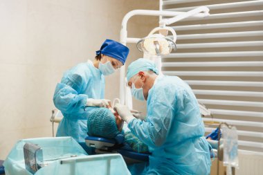 Üniforma ve kadın asistanı erkek eski profesyonel diş hekimi cerrahı Kliniği hafif ofis modern araçlar ekipman ile işlem yükleme diş implant diş kadın hastanın gerçekleştirmek için yardımcı olur.