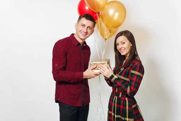 Beautiful young happy smiling couple in love. Woman and man holding golden gift boxes with present and red, yellow balloons, celebrating birthday, on white background isolated. Holiday, party concept. — Stock Photo, Image