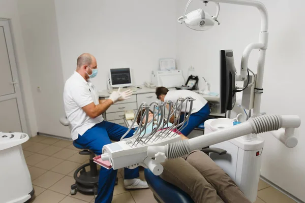 Proceso de preparación e instalación de corona de cerámica dental. El dentista profesional masculino y el asistente femenino ayudan a tratar los dientes de la paciente en la oficina ligera clínica con equipos de herramientas modernos . —  Fotos de Stock