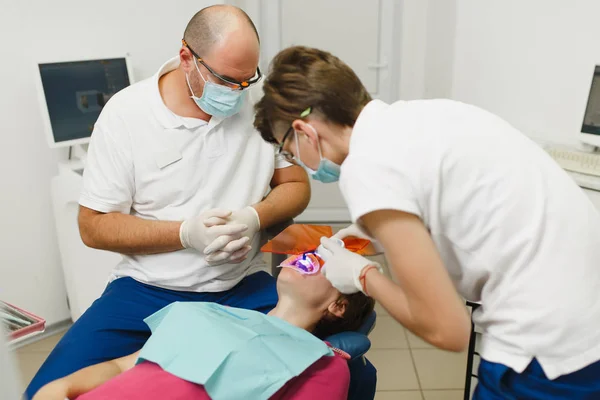 Processen för tandblekning UV-lampa med fotopolymer sammansättning. Professionell tandläkare och kvinnlig assistent hjälper behandla tänderna av kvinnlig patient på klinik ljus kontor med moderna verktyg utrustning. — Stockfoto