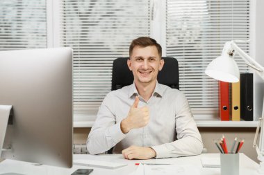 Yakışıklı iş adamı masada oturmuş, bilgisayarda çalışan modern monitör, lamba, klasörler, başparmak, gösterilen gömlek gülümseyen belgelerde ofis pencere arka plan üzerinde ışık. Yöneticisi veya alt.