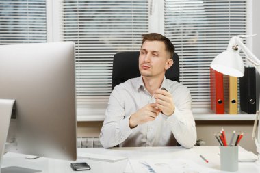 Pencere arka plan üzerinde ışık ofiste masa başında oturan gömlek ciddi ve dalmış iş adamı ile modern monitör, klasörler, kahve ya da çay, bilgisayarda çalışan makaleler. Yöneticisi veya alt.