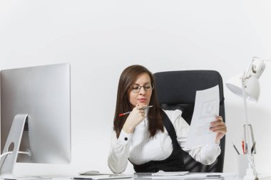 Takım elbise ve masa başında oturan gözlük güzel ciddi ve dalmış Kahverengi saç iş kadını bilgisayar başında beyaz zemin üzerine ışık Office belgeleri ile modern İzleyicisi ile çalışma