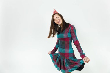 Güzel beyaz eğlenceli kutluyor ve zevk mutlu kadın ekose elbise ve doğum günü parti şapkası utangaç çekici gülümseme ve kahverengi saç, tatil için reklam izole beyaz arka plan üzerinde.