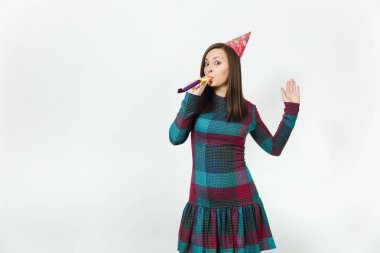 Güzel beyaz eğlence genç mutlu kadın ekose elbise ve doğum günü parti şapkası ile utangaç çekici gülümseme ve boru, kutlama ve reklam için izole beyaz arka plan üzerinde tatil keyfini.