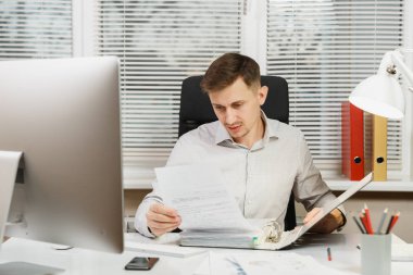 Bilgisayarda çalışan modern monitör, kırmızı klasör, belge penceresi arka plan üzerinde ışık Office ile yakışıklı ciddi ve dalmış iş adamı masa başında oturan gömlek. Yöneticisi veya alt.