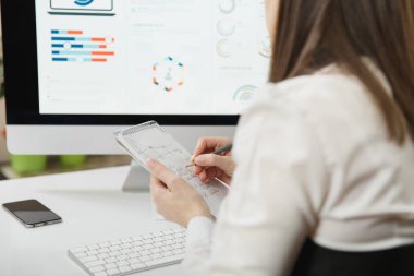 Masa başında oturan takım elbiseli Brown-saç iş kadını kalem bilgi ile defter için bilgisayarda çerçevede modern monitör, geri ışık Office belgeleri ile çalışan görünüm yazma