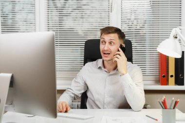 Masa başında oturan gömlek gülümseyen iş adamı hoş sohbet, bilgisayar başında modern monitör, belge penceresi arka plan üzerinde ışık ofiste çalışan iletken cep telefonda konuşurken.
