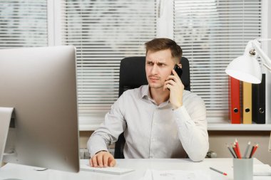Cep telefonu üzerinde konuşurken ciddi iş adamı masa başında oturan gömlek sorunları, bilgisayar başında modern monitör, belge penceresi arka plan üzerinde ışık ofiste çalışan çözümleniyor. Yöneticisi veya alt