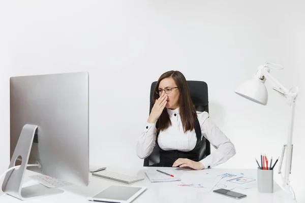 Красива втомлена стресово-коричнева ділова жінка з головним болем, що сидить за столом, працює на сучасному комп'ютері з сучасним монітором з документами у світлому офісі, на білому тлі — стокове фото