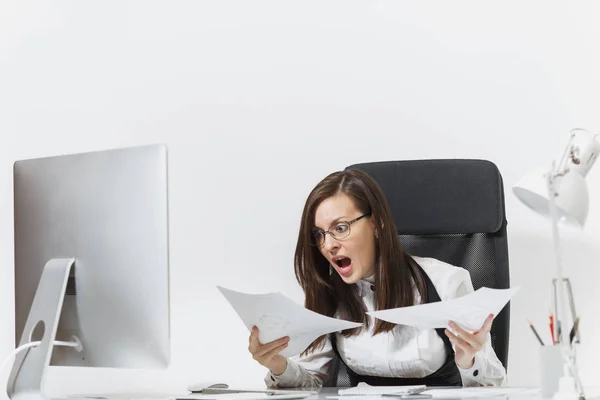 Pretty angry business woman in suit sitting at the desk with documents, working at computer with modern monitor in light office, swearing and screaming, resolving issues, on white background — Stock Photo, Image