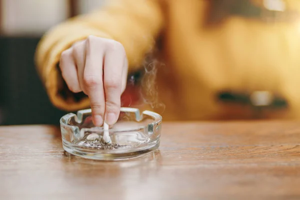 Εστίαση στο χέρι καυκάσιος γυναίκα βάζει έξω το τσιγάρο στο τασάκι με γυαλί στο ξύλινο τραπέζι, αποτσίγαρο, κάπνισμα πεθαίνει. Σταματήσουν το κάπνισμα. Έννοια της υγείας. Εσωτερικη φωτογραφία. — Φωτογραφία Αρχείου