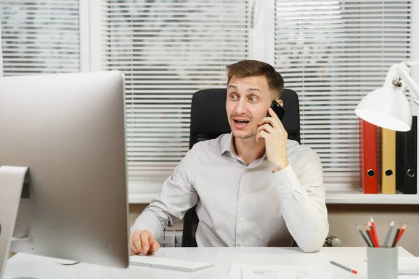 Masa başında oturan gömlek gülümseyen iş adamı hoş sohbet, bilgisayar başında modern monitör, belge penceresi arka plan üzerinde ışık ofiste çalışan iletken cep telefonda konuşurken.