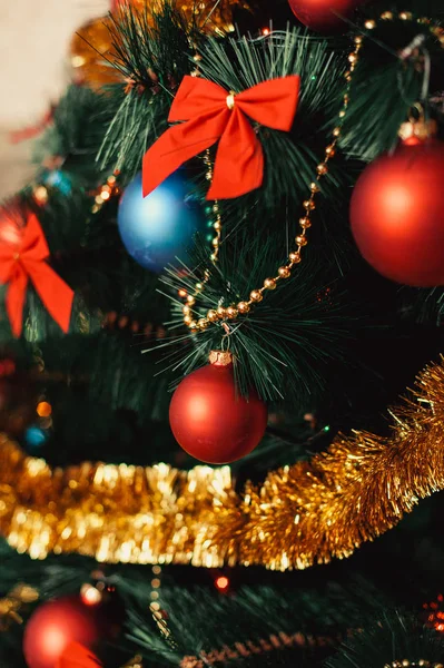 Закройте елку украшения из стекла с цветными красными, голубыми шариками, золотой мишурой, красными луками, золотыми нитками из бусин с блестками и теплыми деталями освещения. Концепция Нового года и праздника 2018 . — стоковое фото
