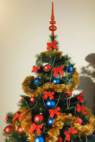 Beautiful Christmas tree ornaments made of glass with colored red, blue balls, golden tinsel, red bows, golden strings of beads with glitter and warm lighting detail. New Year and holiday 2018 concept — Stock Photo, Image