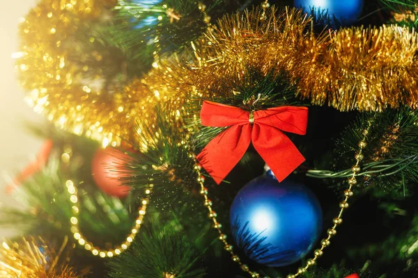 Закройте елку украшения из стекла с цветными красными, голубыми шариками, золотой мишурой, красными луками, золотыми нитками из бусин с блестками и теплыми деталями освещения. Концепция Нового года и праздника 2018 . — стоковое фото