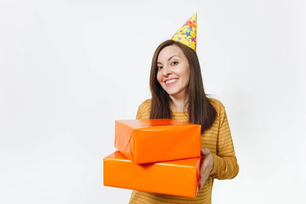Bonita mulher feliz branca divertida jovem em roupas amarelas, chapéu de festa de aniversário segurando caixas de presente laranja com presente, celebrando e desfrutando de férias em fundo branco isolado para propaganda . — Fotografia de Stock