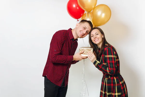 Beautiful young happy smiling couple in love. Woman and man holding golden gift boxes with present and red, yellow balloons, celebrating birthday, on white background isolated. Holiday, party concept. — Stock Photo, Image