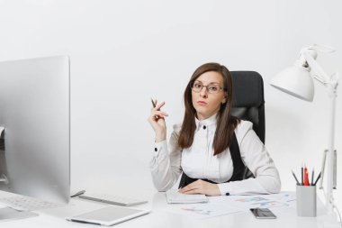 Takım elbise ve masa başında oturan gözlük güzel ciddi ve dalmış Kahverengi saç iş kadını bilgisayar başında beyaz zemin üzerine ışık Office belgeleri ile modern İzleyicisi ile çalışma