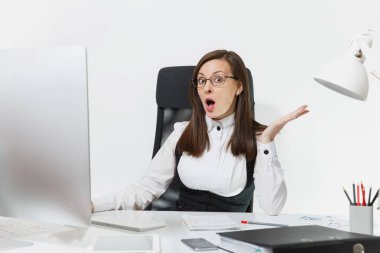 Modern monitör ve beyaz arka plan üzerinde ışık office belgelerinde bilgisayarda çalışma oldukça şaşırmış şaşkın Kahverengi saç iş kadını takım elbise ve masa başında oturan gözlük açık ağızlı