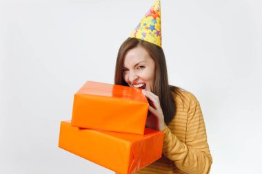 Beyaz eğlence genç deli kadın sarı giysiler, doğum günü parti şapka holding, kemiren ve beyaz arka plan üzerinde mevcut, kutluyor tatil turuncu hediye kutuları ısırma reklam için izole.