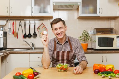 Tavuk ve Bıldırcın yumurta, sebze salatası ışık mutfakta holding beyaz yakışıklı genç masadan, önlük, kahverengi gömlekli. Diyet kavramı. Sağlıklı bir yaşam tarzı. Evde yemek. Yemek hazırlamak