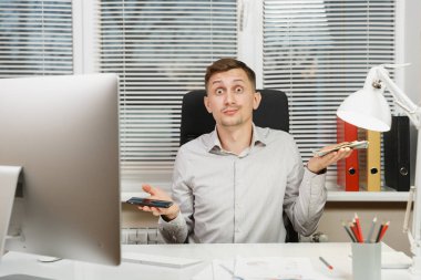 Çalışma ile modern sınıf başkanı bilgisayar, ışık office belgelerinde konusunda düşünceli karışık iş adamı cep telefonu ve çok nakit para arasında seçim yapma masada oturan gömlek. Yöneticisi veya alt.