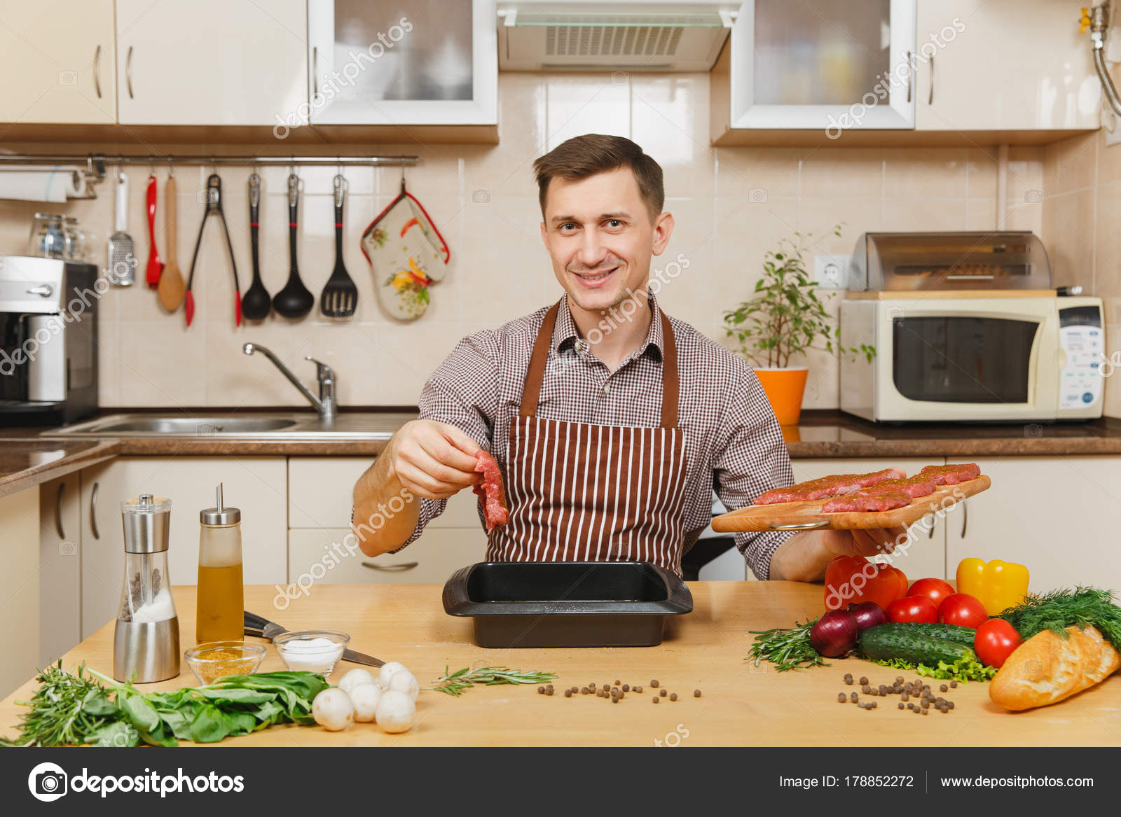 Kaukasische junge Mann Schürze sitzt am Tisch mit Gemüse, Kochen zu ... Kaukasische junge Mann Schürze sitzt am Tisch mit Gemüse, Kochen zu ...