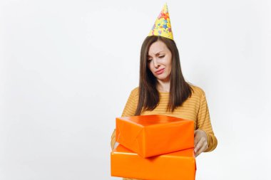Güzel memnun üzgün üzgün kadın sarı giysili, doğum günü parti şapkası ile mevcut, kutluyor kötü tatil turuncu hediye kutuları yalnız beyaz arka planda tutan reklam için izole.