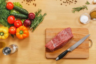 Çiğ et. Farklı sebze, baharat, mantar, peper, dereotu, fesleğen, biberiye, bıçak ile ahşap masa üzerinde kesme tahtası üzerinde taze Dana bonfile. Üstten Görünüm, düz yatıyordu. Kopya alanı reklam için.