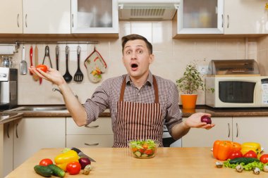 Soğan ve domates, yetişmek sebze salatası arasında ışık mutfakta bıçakla seçme eğlenceli Beyaz delikanlı masadan, önlük, kahverengi gömlekli. Diyet kavramı. Evde yemek. Yemek hazırlamak.