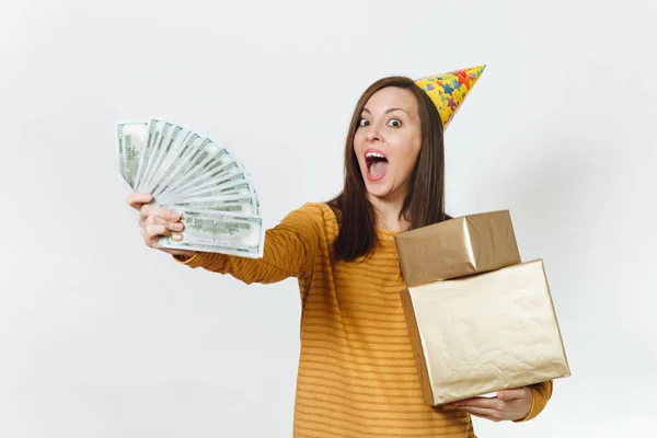 Καυκάσιος διασκέδαση ευτυχισμένη γυναίκα με κίτρινα ρούχα, καπέλο πάρτι γενεθλίων κρατώντας χρυσό δώρο κουτιά με το παρόν και το wad των μετρητών χρημάτων, γιορτάζει Διακοπές σε λευκό φόντο απομονωθεί για διαφήμιση. — Φωτογραφία Αρχείου