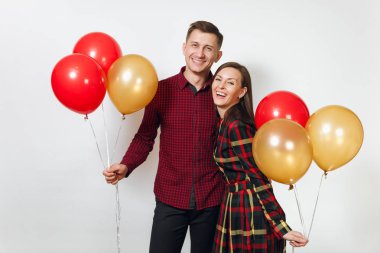 Güzel genç mutlu gülümseyen çift aşık. Kadın ve adam izole beyaz arka plan üzerinde doğum günü kutlama kırmızı, sarı balonları, ekose kareli giysiler içinde. Tatil, parti konsept.