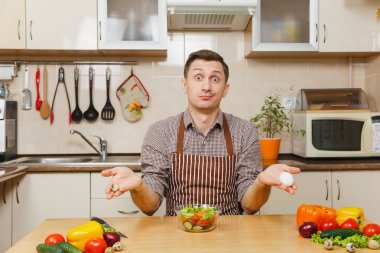 Tavuk ve Bıldırcın yumurta, sebze salatası ışık mutfakta holding beyaz yakışıklı genç masadan, önlük, kahverengi gömlekli. Diyet kavramı. Sağlıklı bir yaşam tarzı. Evde yemek. Yemek hazırlamak