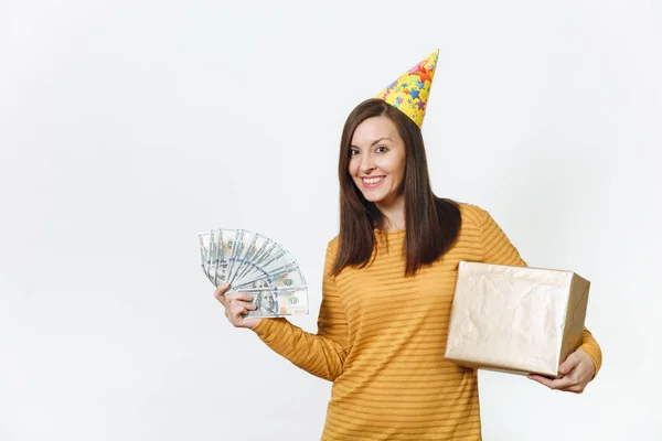 Divertimento caucasico giovane donna felice in abiti gialli, cappello da festa di compleanno con scatola regalo dorata con regalo e mazzetta di denaro contante, festeggiando la vacanza su sfondo bianco isolato per la pubblicità . — Foto Stock