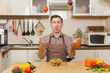 Soğan ve domates, yetişmek sebze salatası kadar ışık mutfak bıçak atma eğlenceli deli beyaz delikanlı masadan, önlük, kahverengi gömlekli. Diyet kavramı. Evde yemek. Yemek hazırlamak.