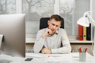 Pencere arka plan üzerinde ışık ofiste masa başında oturan gömlek ciddi ve dalmış iş adamı ile modern monitör, klasörler, kahve ya da çay, bilgisayarda çalışan makaleler. Yöneticisi veya alt.