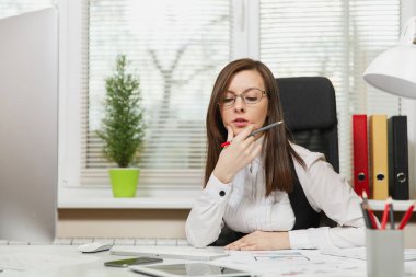Takım elbise ve tablet ile masaya oturan gözlük güzel ciddi ve dalmış Kahverengi saç iş kadını ışık Office belgeleri ile modern monitör bilgisayarda çalışan bir kenara arıyorsunuz