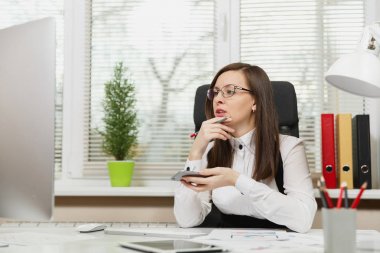 Takım elbise ve cep telefonuyla, Masa başında oturan gözlük güzel ciddi ve dalmış Kahverengi saç iş kadını bir kenara seyir ile modern sınıf başkanı bilgisayar, ışık office belgelerinde çalışan